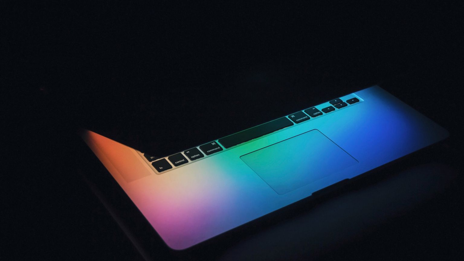 Halb zugeklappter Laptop mit bunten Lichtern, auf dunklem Hintergrund.