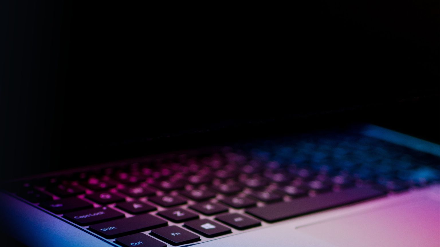 Halb zugeklappter Laptop mit bunten Lichtern, auf dunklem Hintergrund.